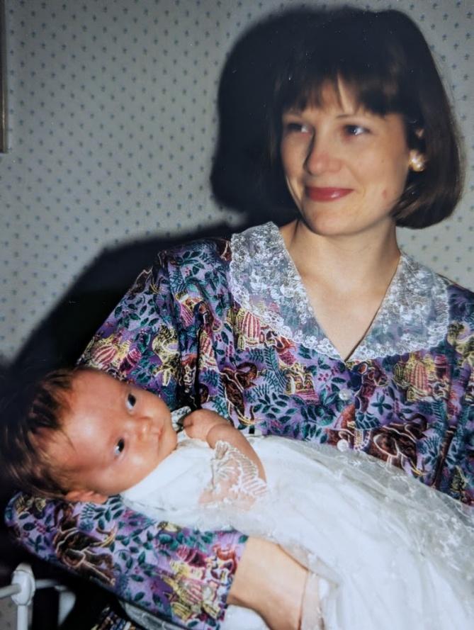 Nicky holding a newborn baby dressed in a long white christening gown