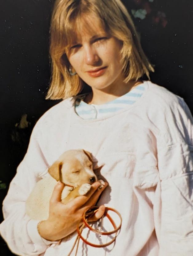 Nicky in a soft pink sweatshirt cradling a small sleeping puppy in her arms