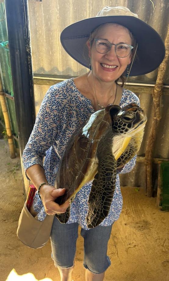 Nicky in a wide-brimmed sun hat, laughing as she holds a large sea turtle